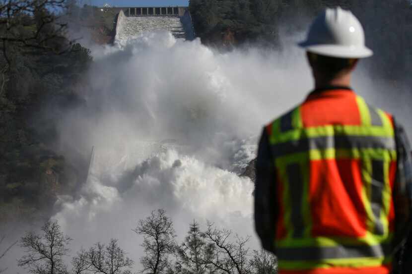 A worker keeps an eye on water coming down the damaged main spillway of the Oroville Dam on...