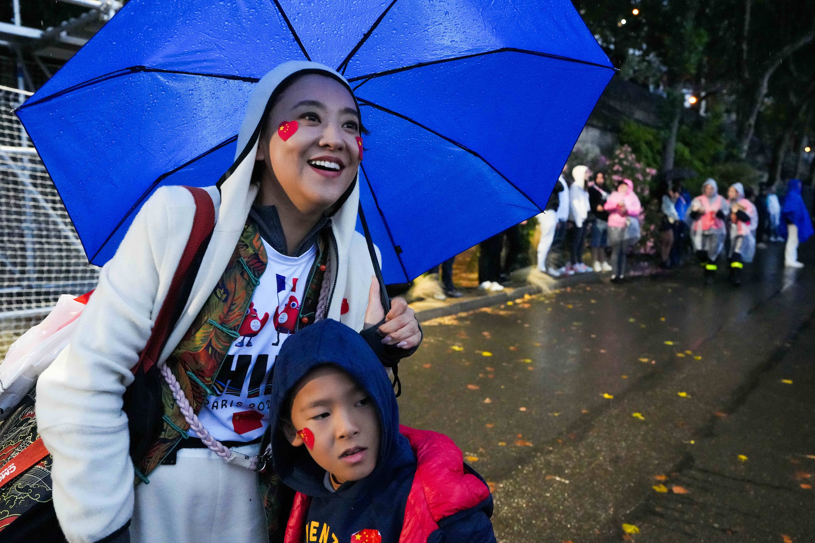 Spectators huddle under umbrellas as they watch along the banks of the Seine during opening...