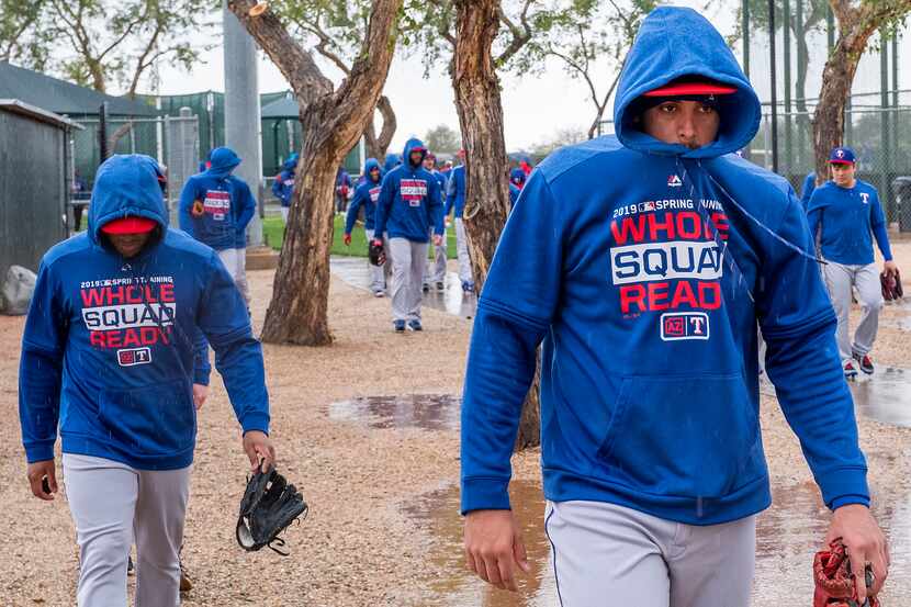 Texas Rangers infielder Ronald Guzman (right) bundles up against a cold rain while walking...