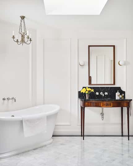 White bathroom, freestanding bathtub, picture frame molding on the walls and an antique...