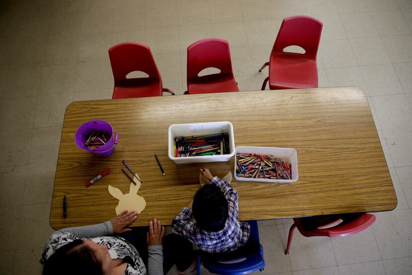 Preschool teacher Arene Galirza, left, and a 4-year-old student color a rabbit-shaped paper...