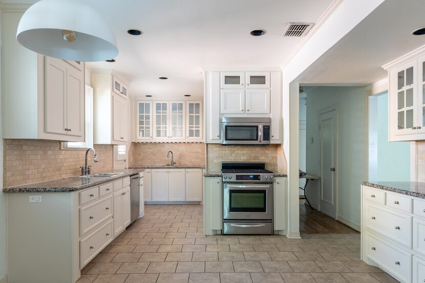 Open kitchen interior with brown tile, white cabinets and gray granite countertops