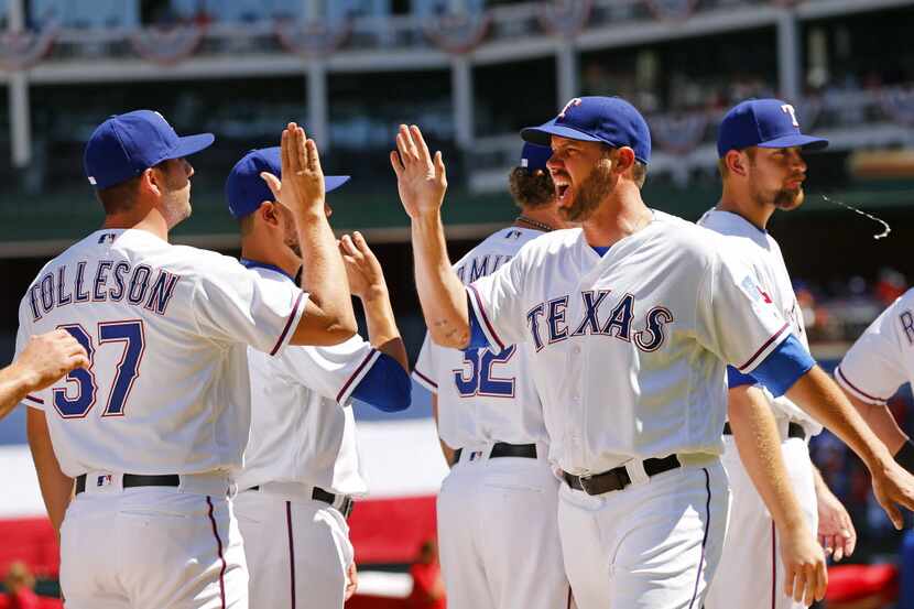 Texas Rangers starting pitcher Colby Lewis (48) slaps hands with teammates after being...
