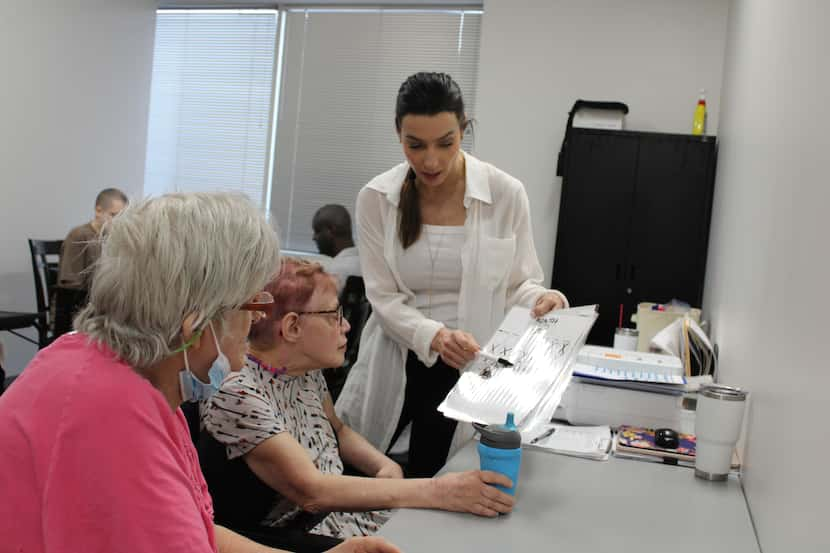 A woman in a white shirt helps two disabled adults with a project.