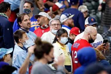 Texas Rangers fans, some with and without masks watch an exhibition game in the seventh...