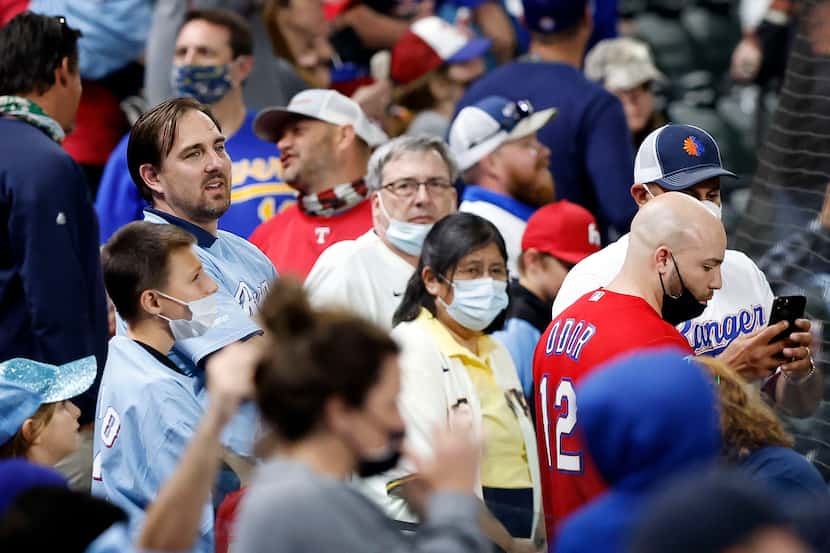 Texas Rangers fans, some with and without masks watch an exhibition game in the seventh...