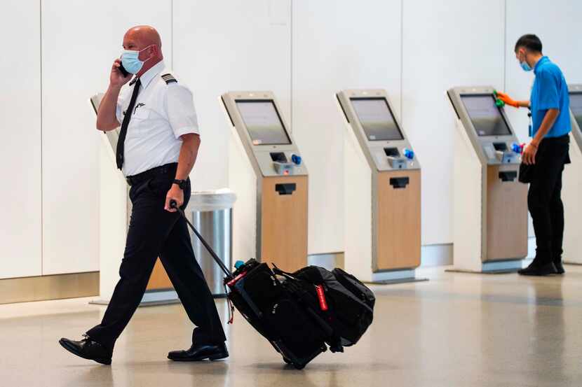 An American Airlines pilot walks past as airport contractor David Ramirez wipes down check...