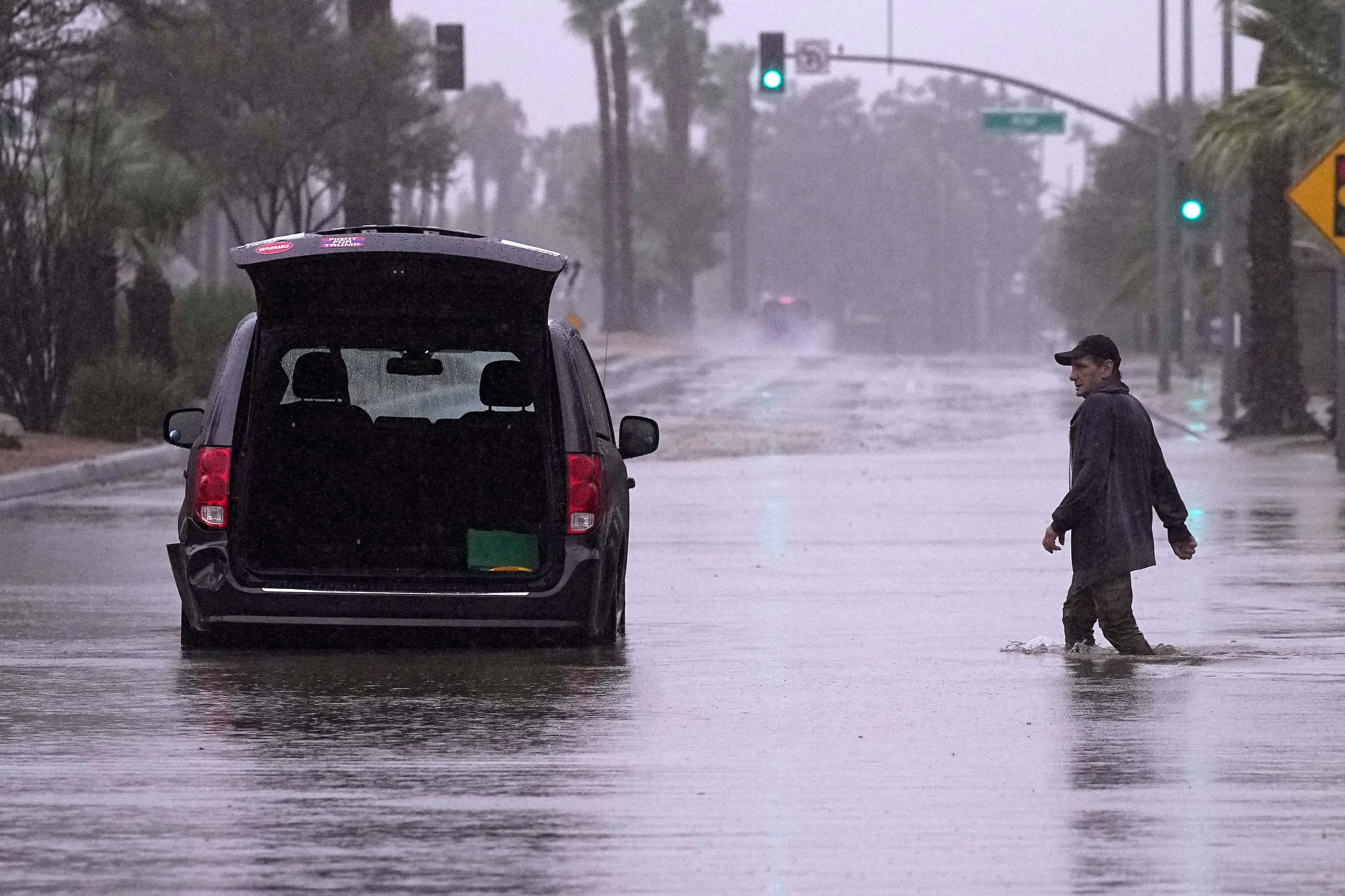 A motorist walks out to remove belongings from his vehicle after becoming stuck in a flooded...