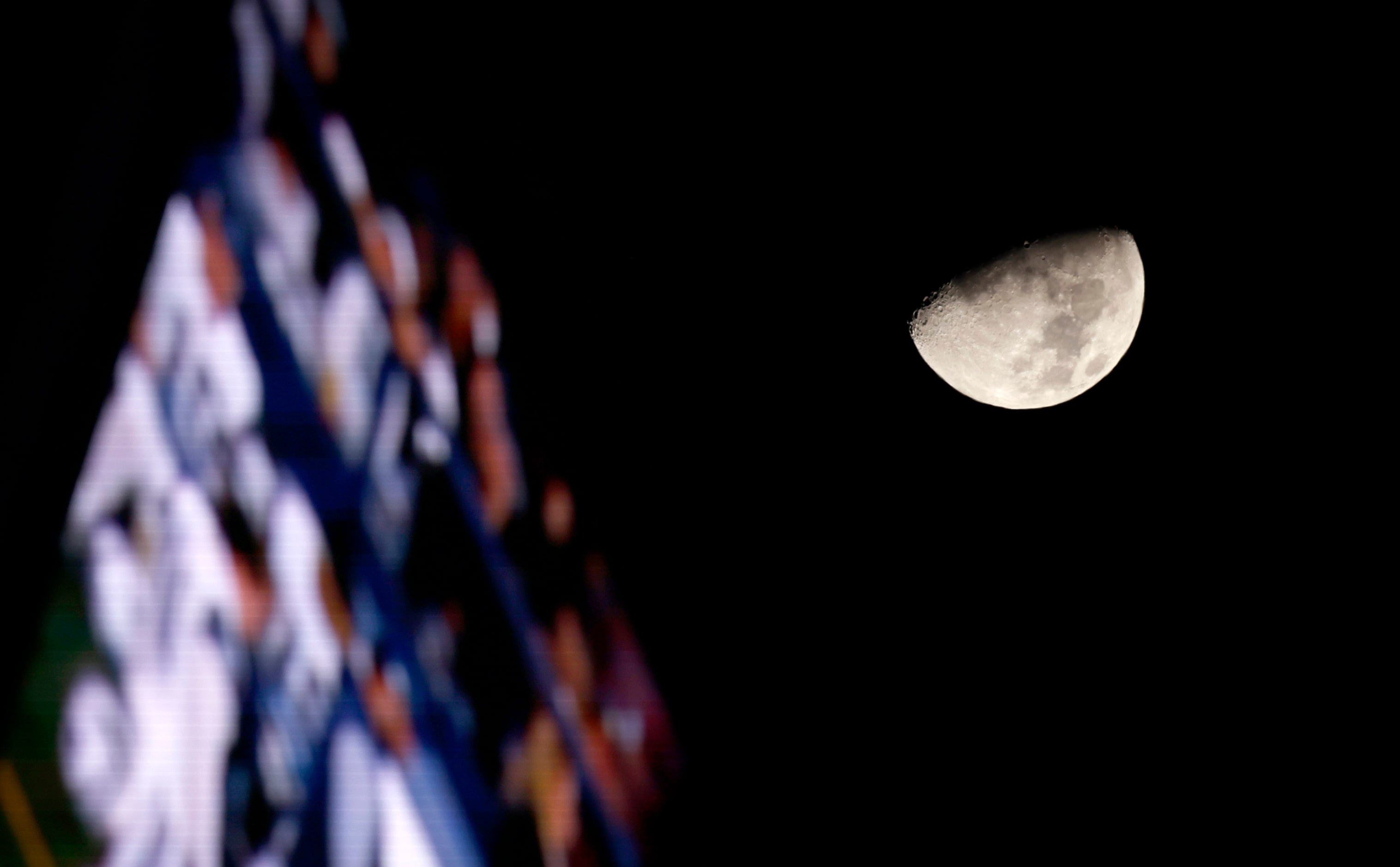 The moon is seen past the video board and through the open roof of AT&T Stadium during the...