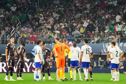 Players for the United States and Mexico stand on the field after play was paused in the...