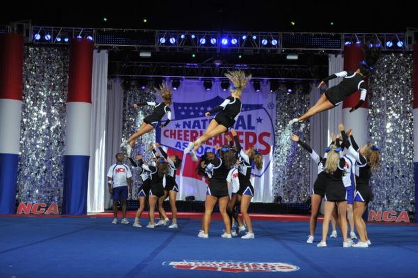 
Cheer team members engage in a choreographed mid-air spin as their teammates prepare to...