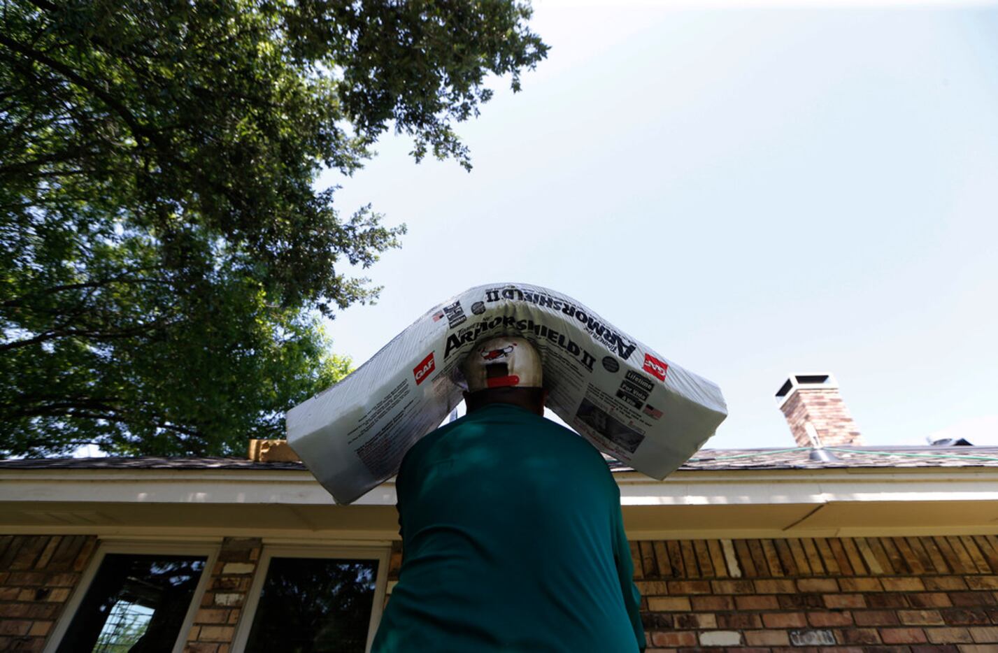 A worker hauls shingles up to a roof on a house in Arlington. Drinking lots of water, taking...