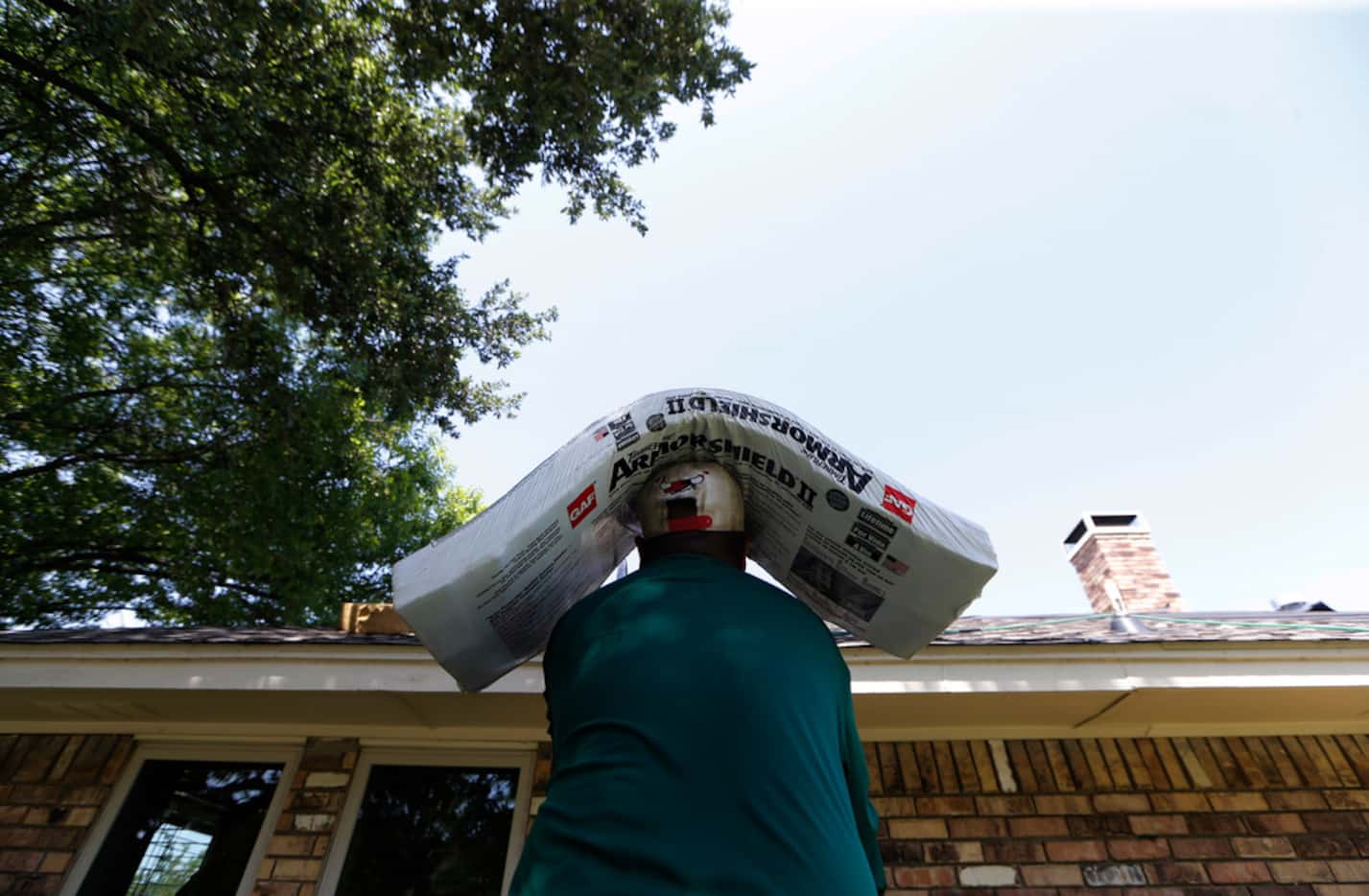 A worker hauls shingles up to a roof on a house in Arlington. Drinking lots of water, taking...