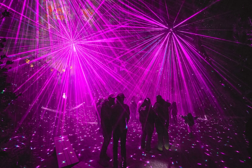 Various people miss around an outdoor area surrounded by bursts of purple laser lights.