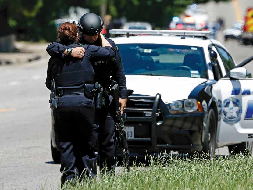 Two Dallas police officers comfort each other at a shooting scene on Dolphin Road where a...