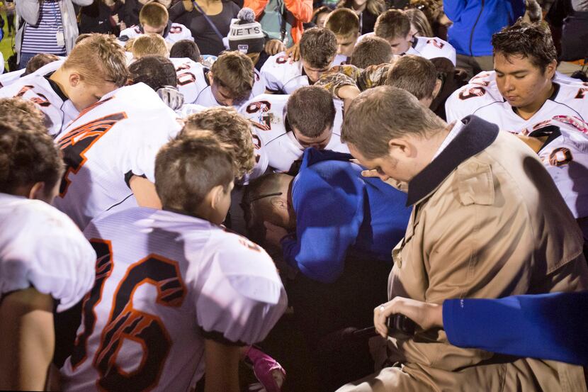 Bremerton High School assistant football coach Joe Kennedy (center in blue) kneels and prays...