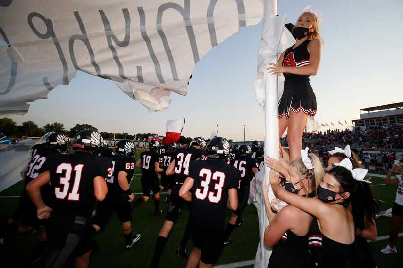 Argyle cheerleaders wear masks while holding a banner that Argyle football players ran...