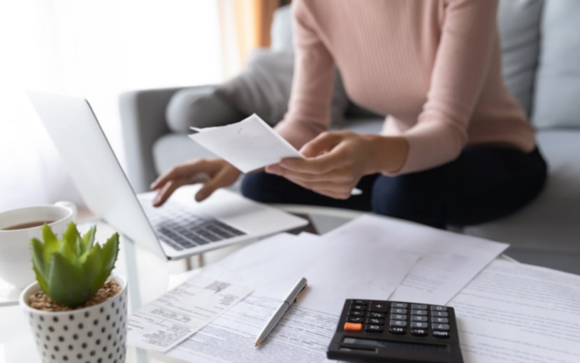 A close up of a woman calculating bills and using a laptop.