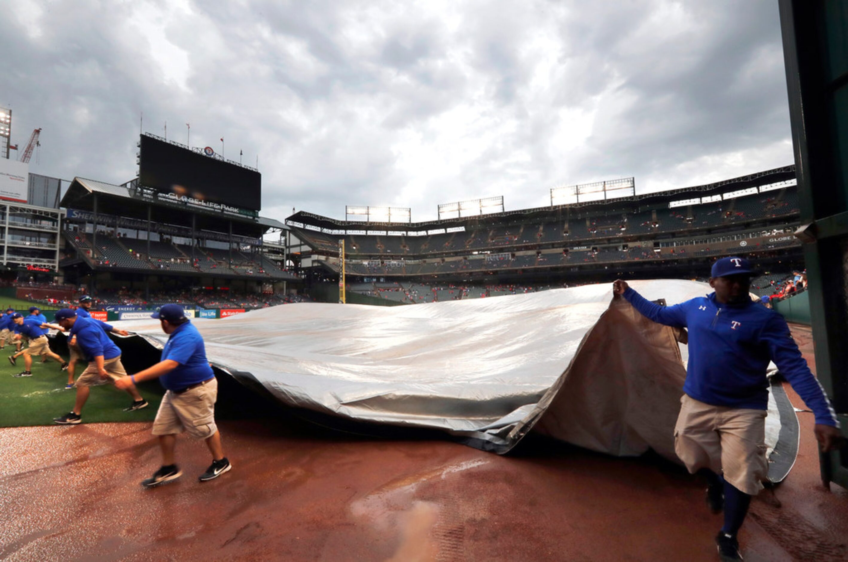 Texas Rangers grounds crew members drag the tarp off the field and onto the outfield after...