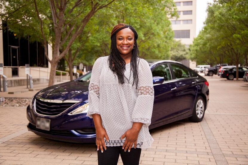 A smiling woman stands in front of a blue car.