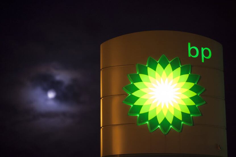 Clouds partially cover the moon beyond an illuminated BP logo as it sits on a sign outside a...