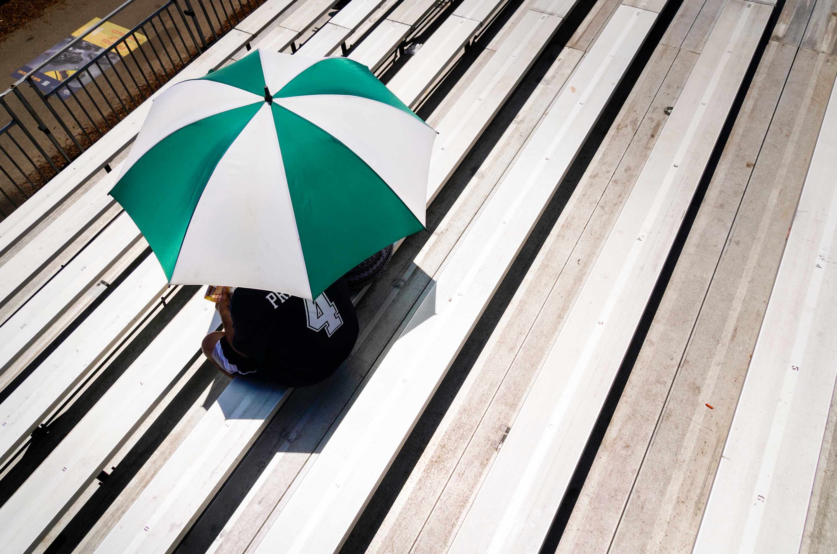 Dallas Cowboys fans find shade under an umbrella as they watch the team practice at training...