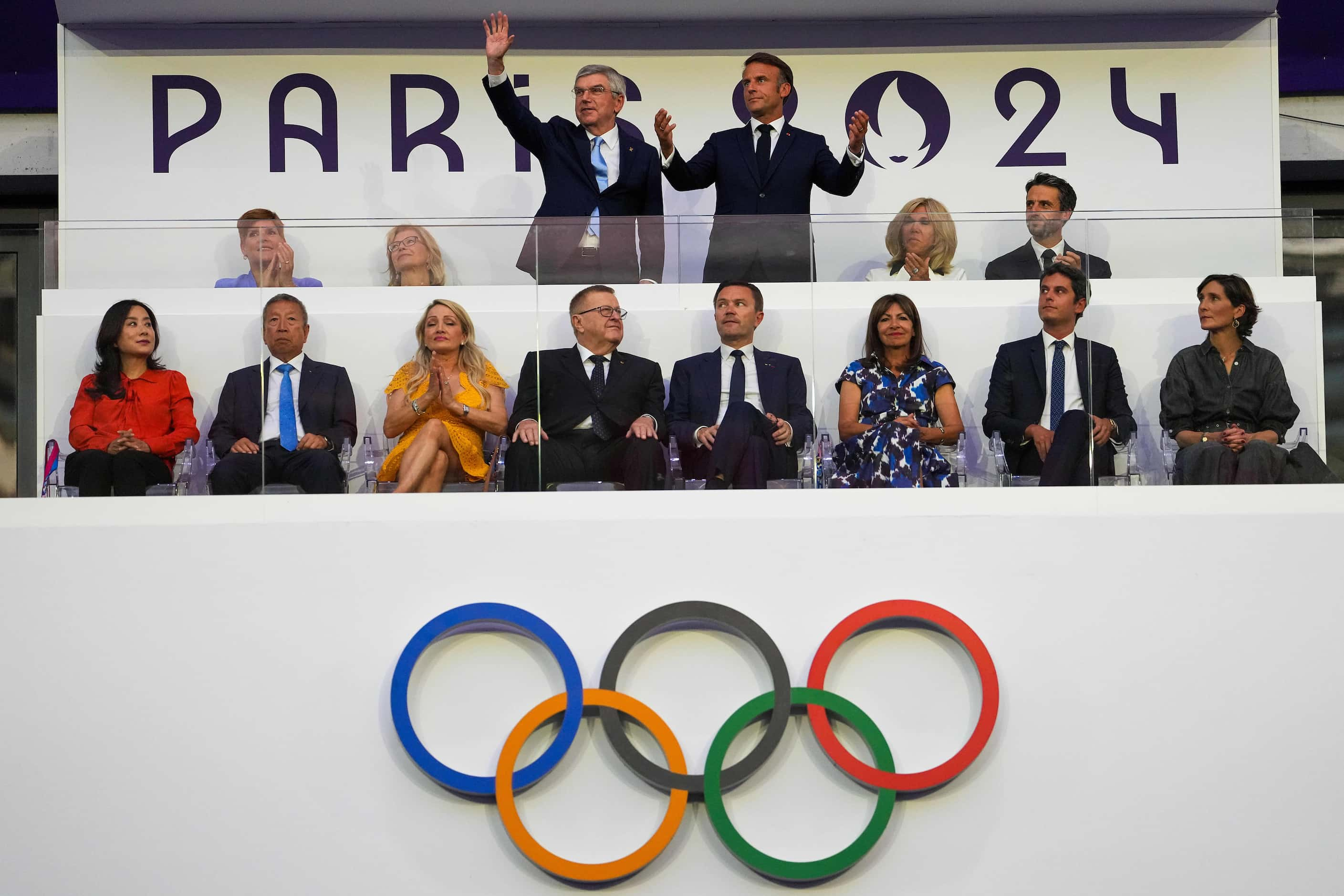 French President Emmanuel Macron (standing top right) and IOC President Thomas Bach wave to...