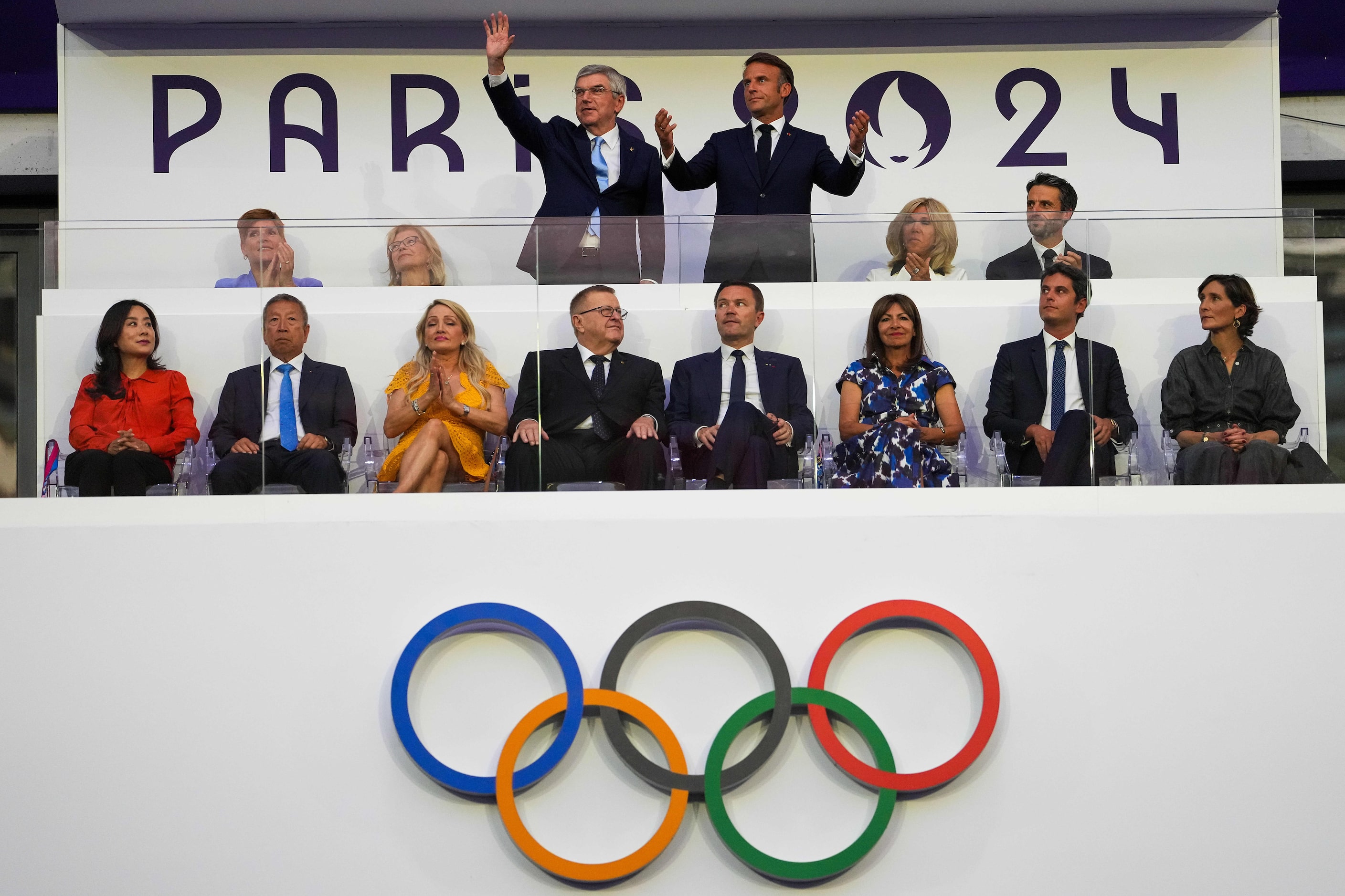 French President Emmanuel Macron (standing top right) and IOC President Thomas Bach wave to...