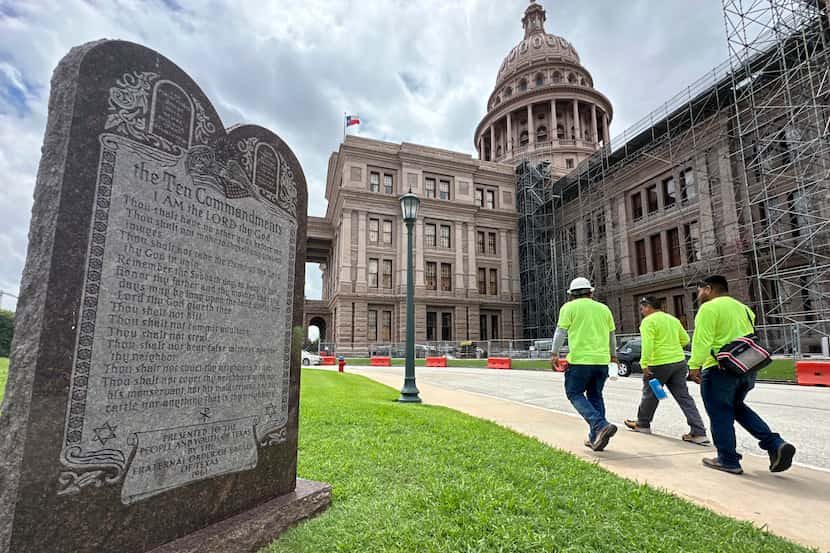 Construction workers walk past a monument of the Ten Commandments outside the Texas Capitol,...