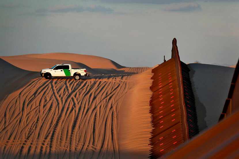 A U.S. Border Patrol agent surveys a section of fence that runs through the Imperial Sand...