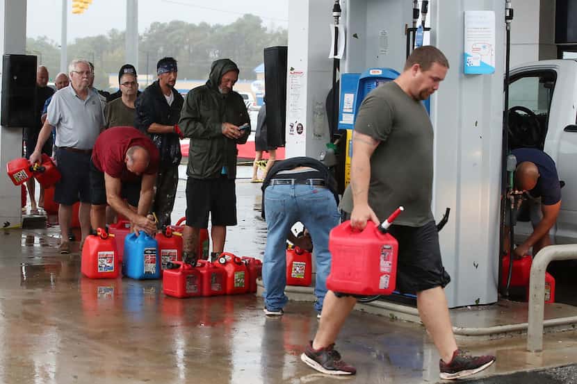 People wait in line to fill gas cans at a gas station that was damaged when Hurricane...
