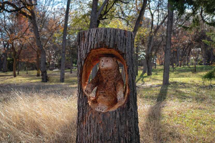 A sculpture of a bear sitting in a tree trunk.