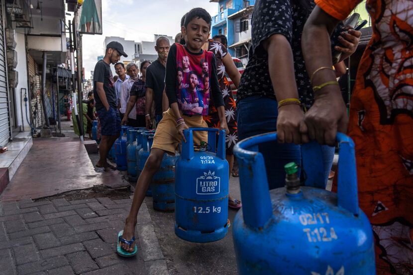 A boy tries to lift an empty cylinder as he along with others wait in a queue to buy...
