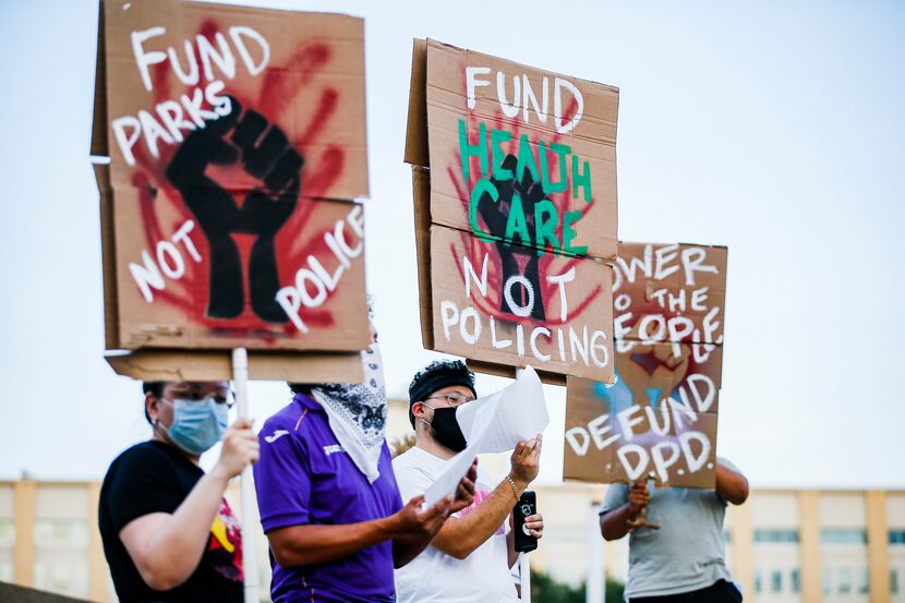 Demonstrators hold up signs demanding that the Dallas Police Departments budget be reduced...