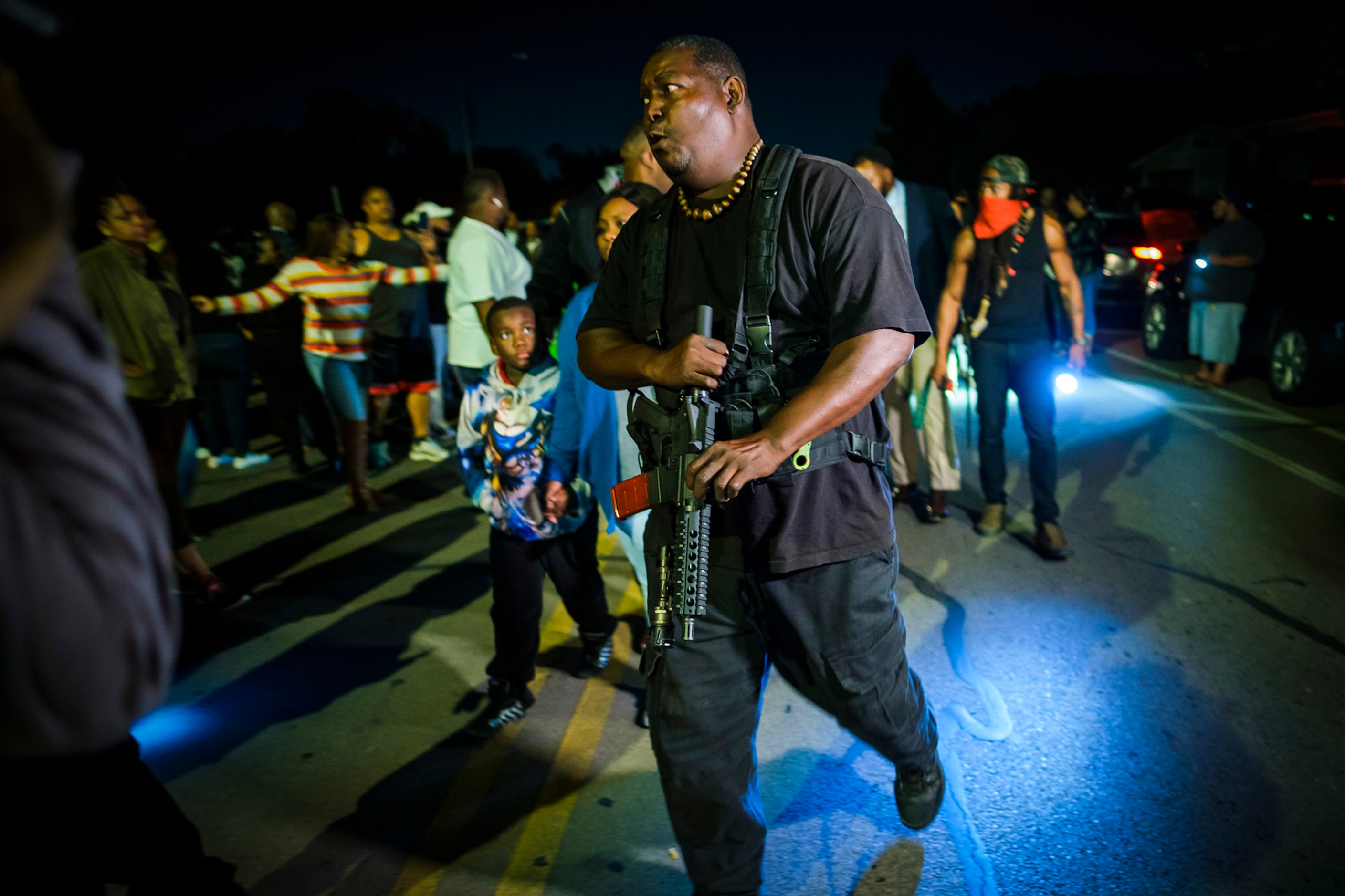 An armed man escort members of the victimÕs family from a community vigil for Atatiana...