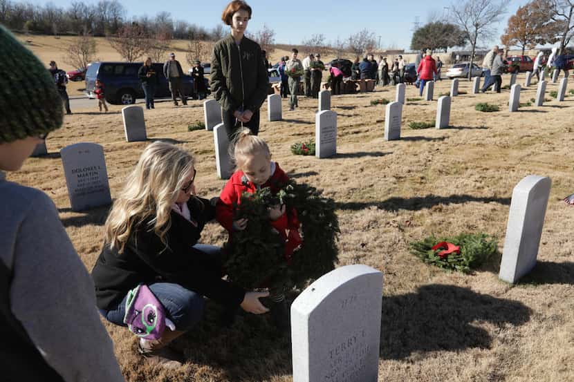 Raylene Moore (left) and 3-year-old Ellie Grace Moore place a wreath as part of a Wreaths...