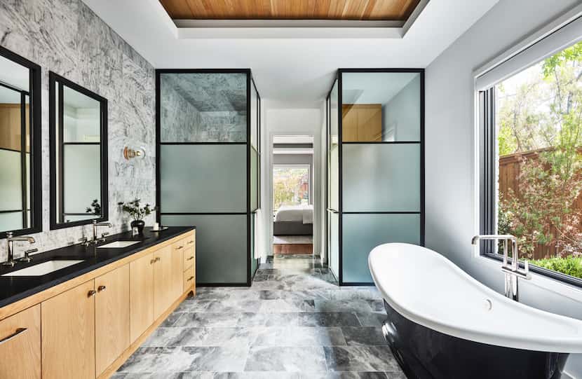 Luxury bathroom with gray flooring, black slipper tub and glass-enclosed shower and water...
