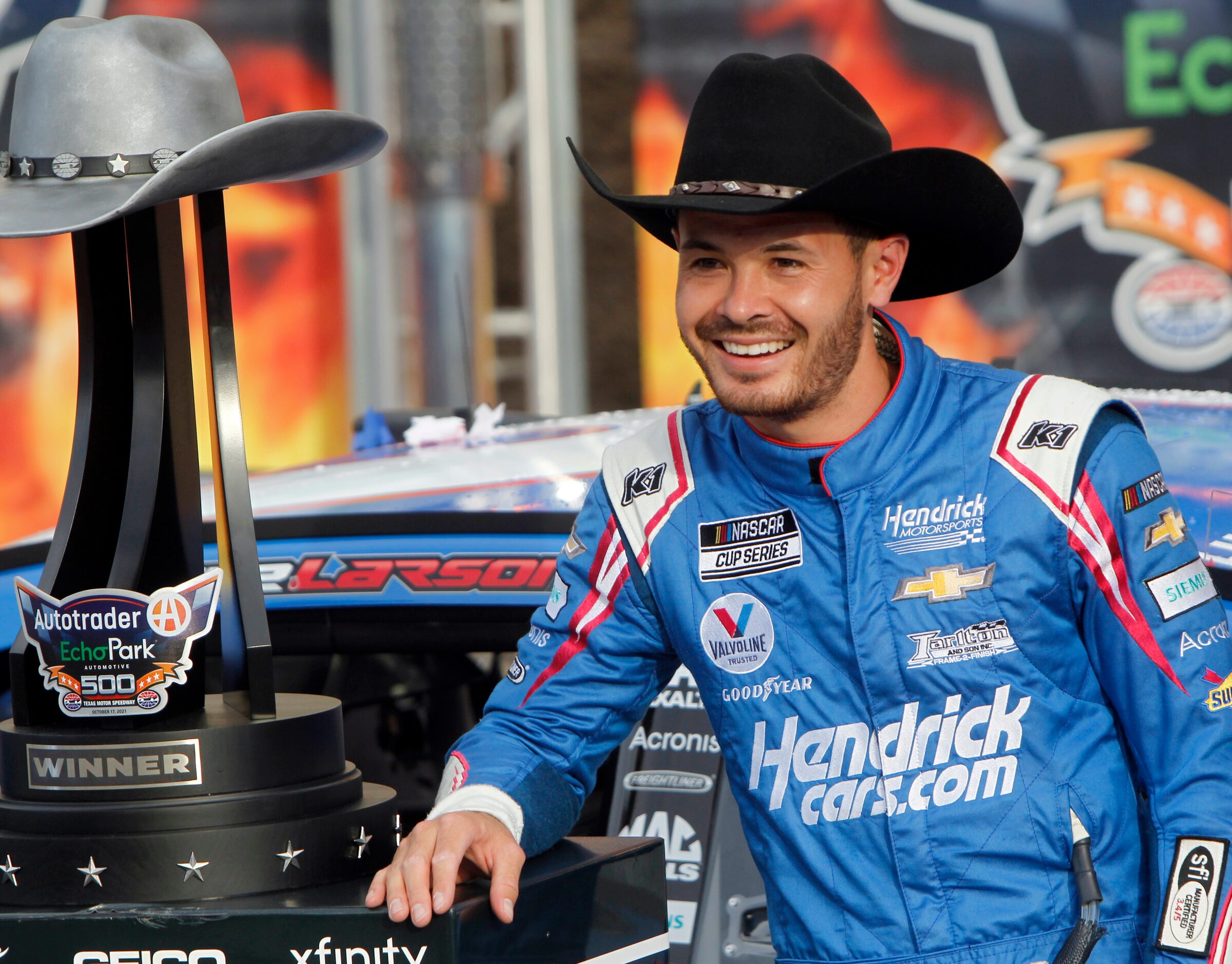 Driver Kyle Larson poses for media cameras after his victory from behind the wheel of the...