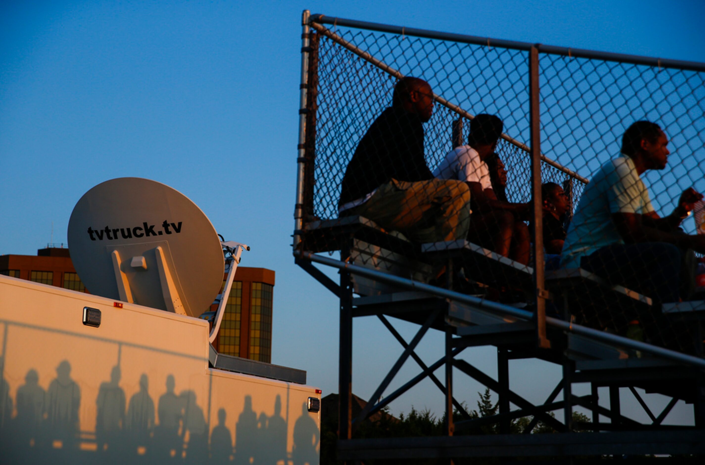 Fan's shadows are cast on an ESPN broadcast satellite truck as the sun sets over a high...