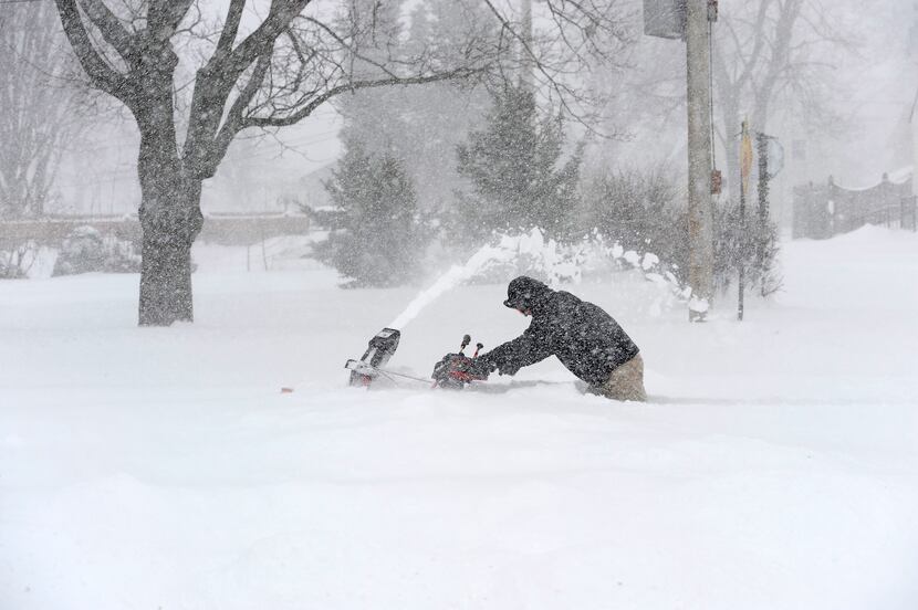 David Colwell steers a snow blower through thigh-deep snow to clear the sidewalk in his...
