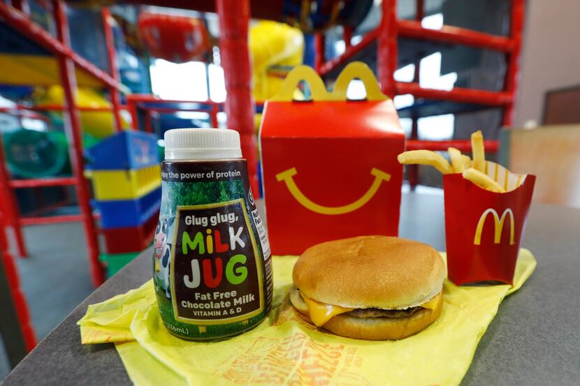 A Happy Meal featuring non-fat chocolate milk and a cheeseburger with fries, are arranged...