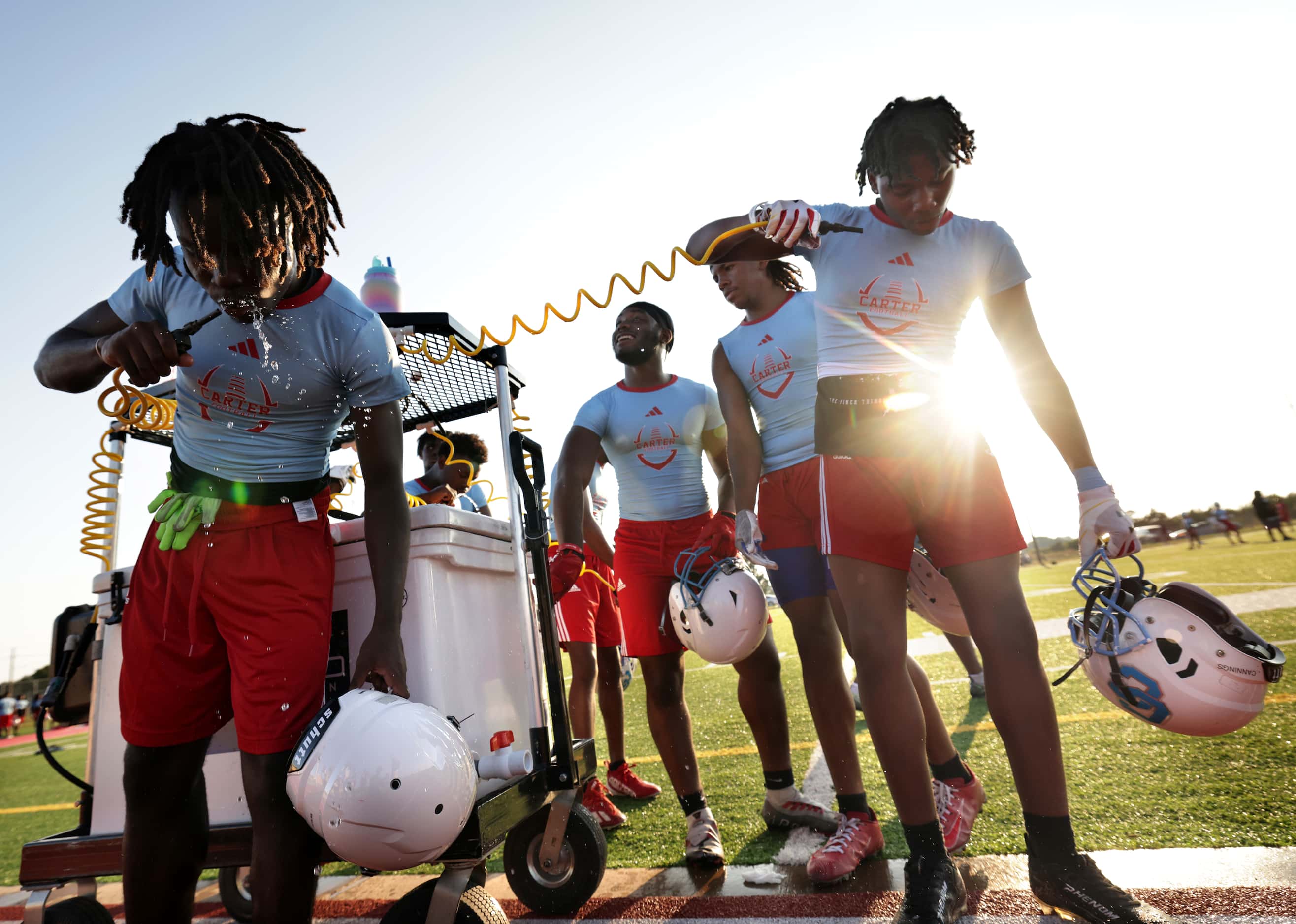 Players get a drink as they attend their first day of football practice at Carter High...
