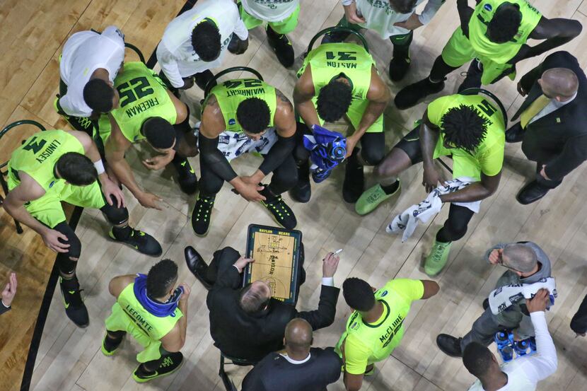 The Baylor team listens intently as head coach Scott Drew draws up a play during a timeout...