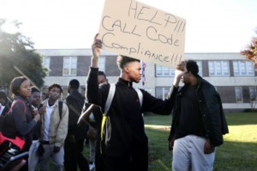  Eleventh-grader Kameron Davis held up a "Help!!! Call Code Compliance!!!" sign during the...