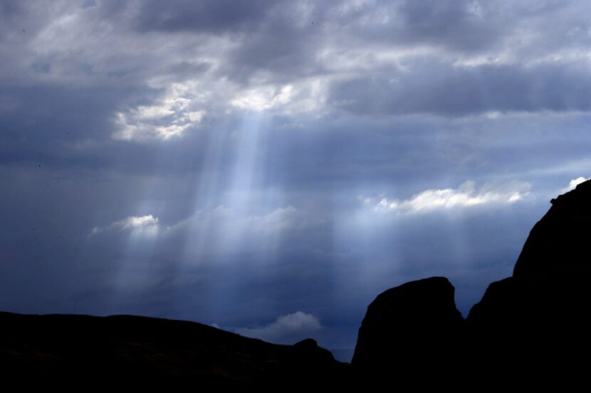 Rays of light stream through the storm clouds over the formations in the Monument Valley,...