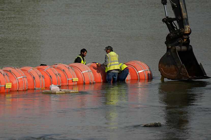Workers made adjustments to buoys being used as a barrier along the Rio Grande in Eagle Pass...