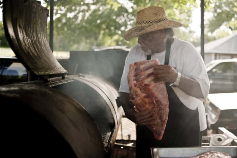 Pit master Clyde Biggins hoists a rack of pork ribs onto his largest smoker in front of his...