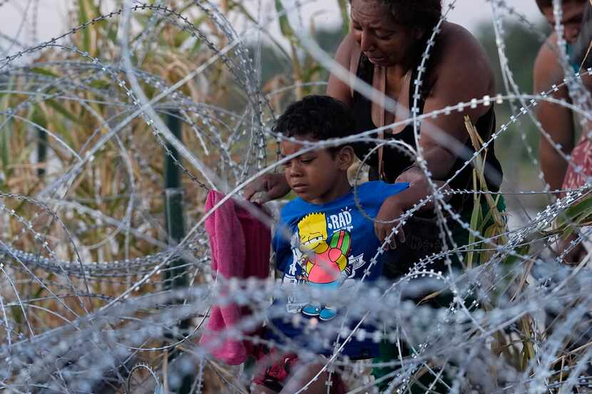 Migrants climb through concertina wire after they crossed the Rio Grande and entered the...