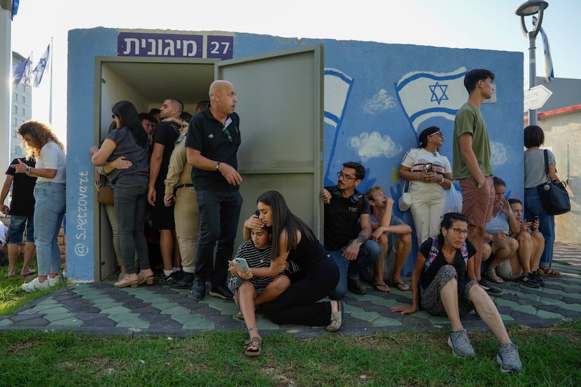 Israelis take cover next to a shelter as a siren sounds a warning of incoming rockets fired...