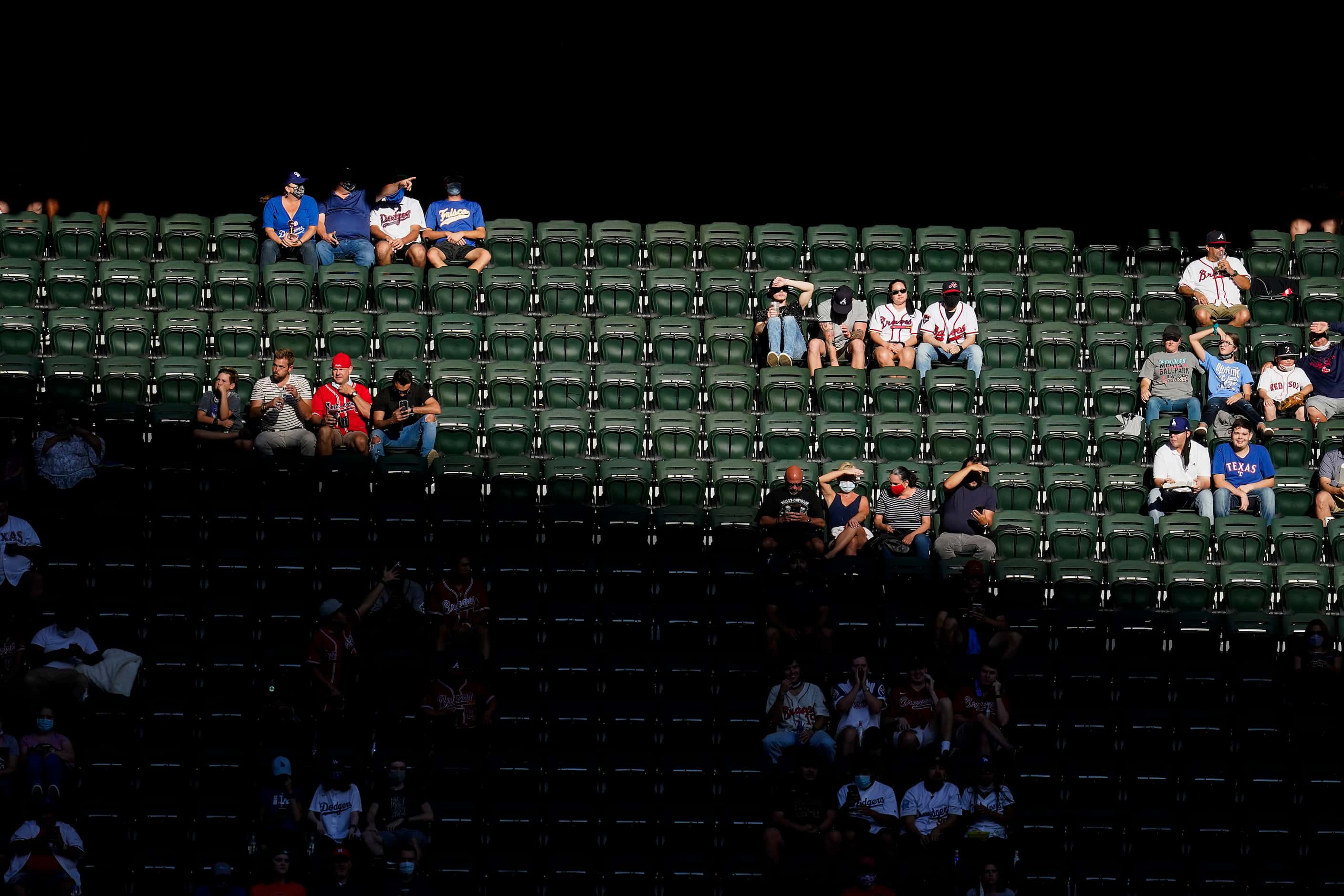 Fans sit socially distanced in the right field stands as sunlight falls over the stadium...